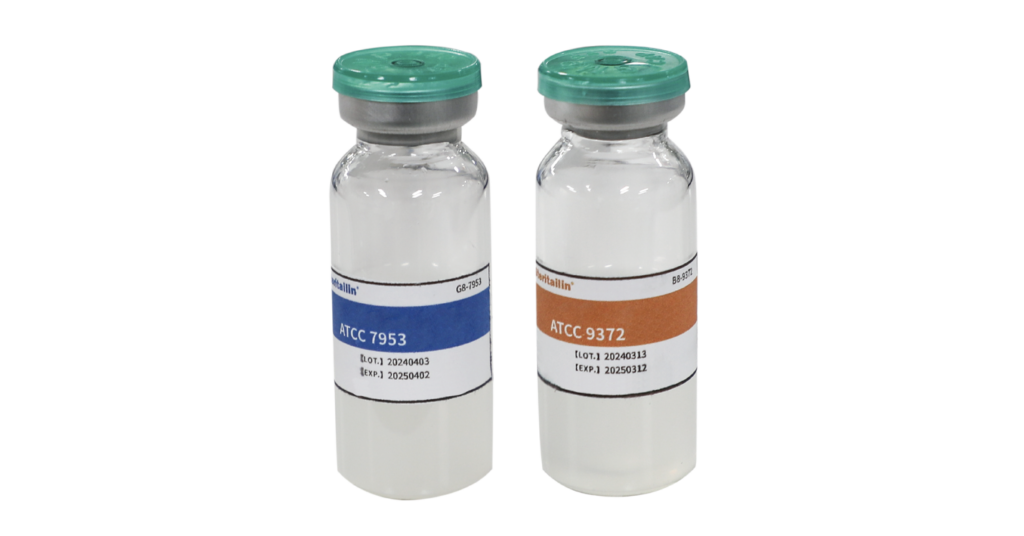 Two glass vials with green caps containing clear liquid; left labeled ATCC 7953 (blue band), right labeled ATCC 9372 (orange band).