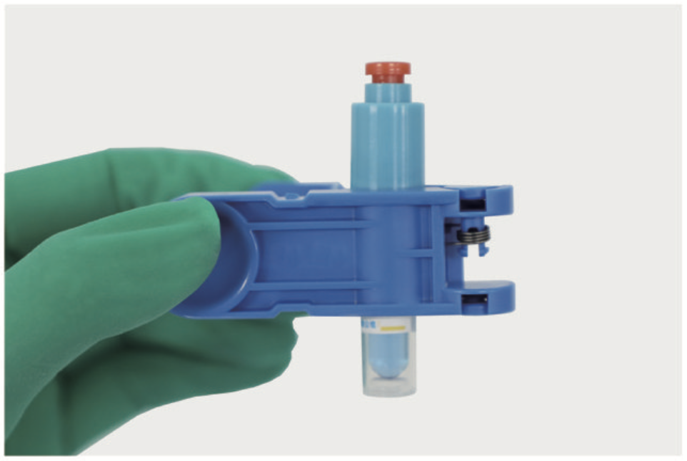 Gloved hand holding a blue plastic medical device with a small vial attached underneath.
