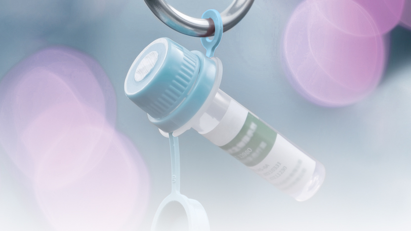 Vaccine or medication vial hanging from a metal ring against a soft, blurred pastel background.
